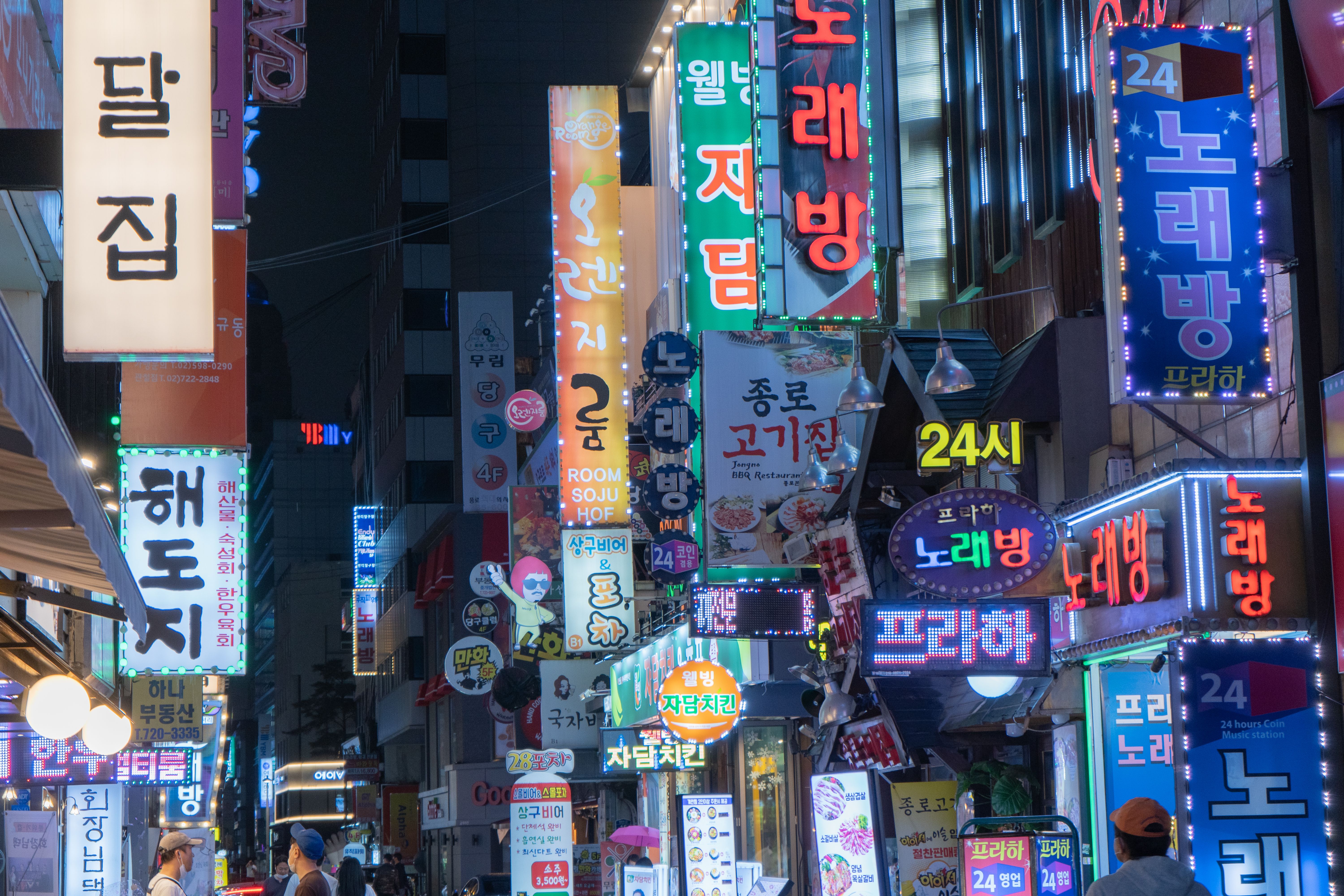 A busy street at night in South Korea, crowded with brightly lit, multi-colored vertical business signs featuring Korean text